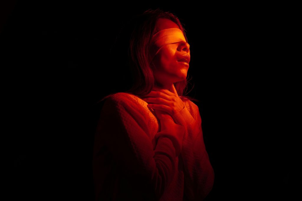 Artistic portrait of a woman in darkness with red light, conveying emotion and mystery.