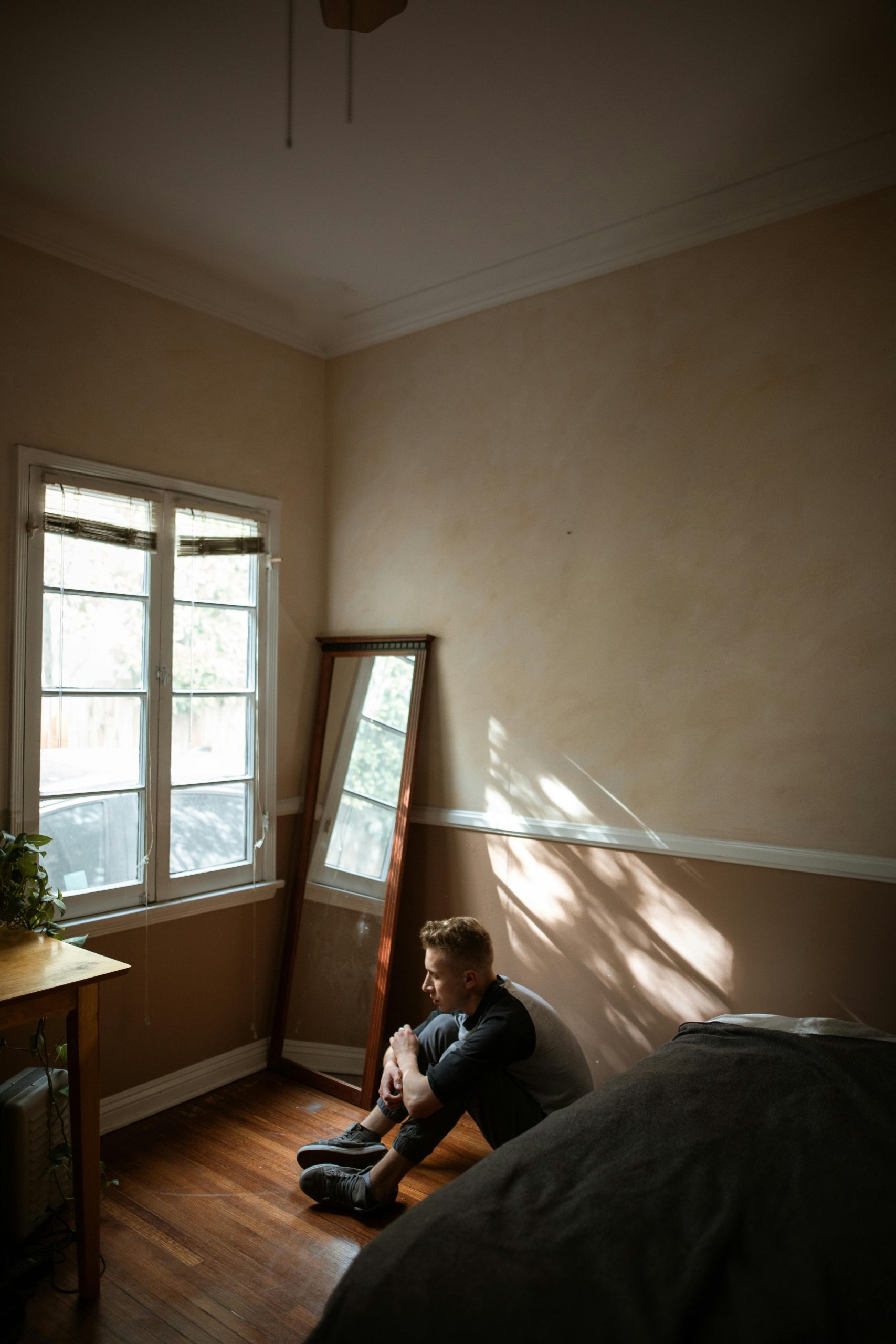 A young man sits alone on the floor, contemplating in a softly lit room.