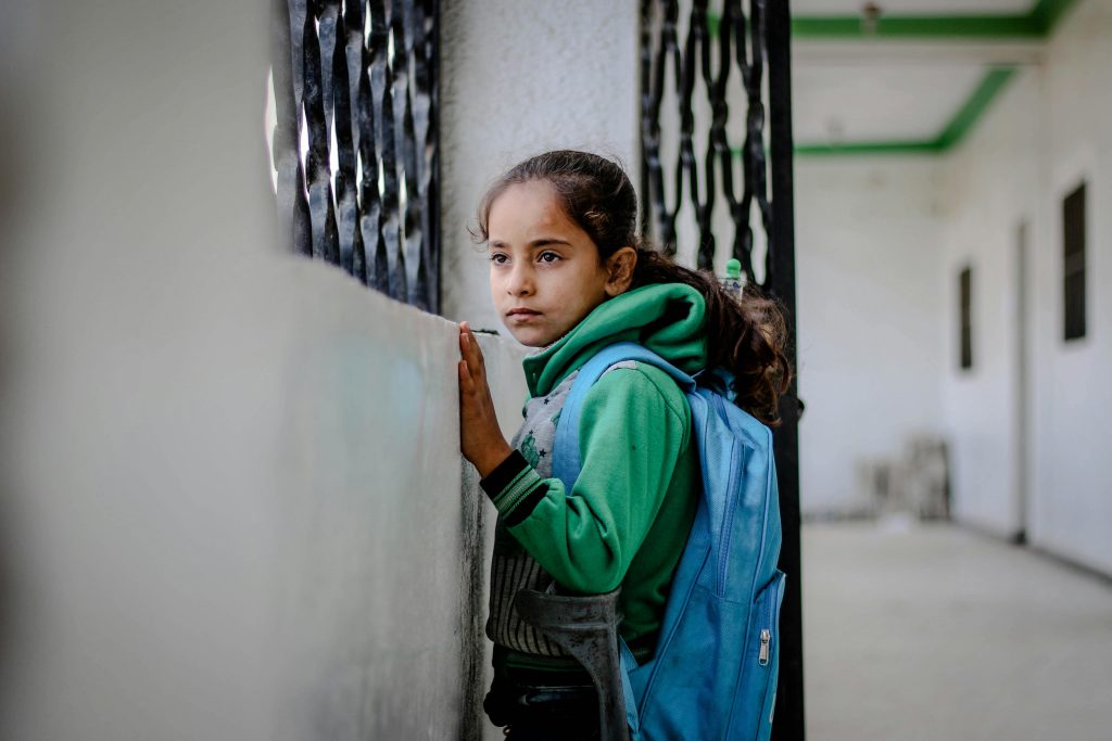 Side view of ethnic girl leaning on concrete wall with window and metal lattice while looking away