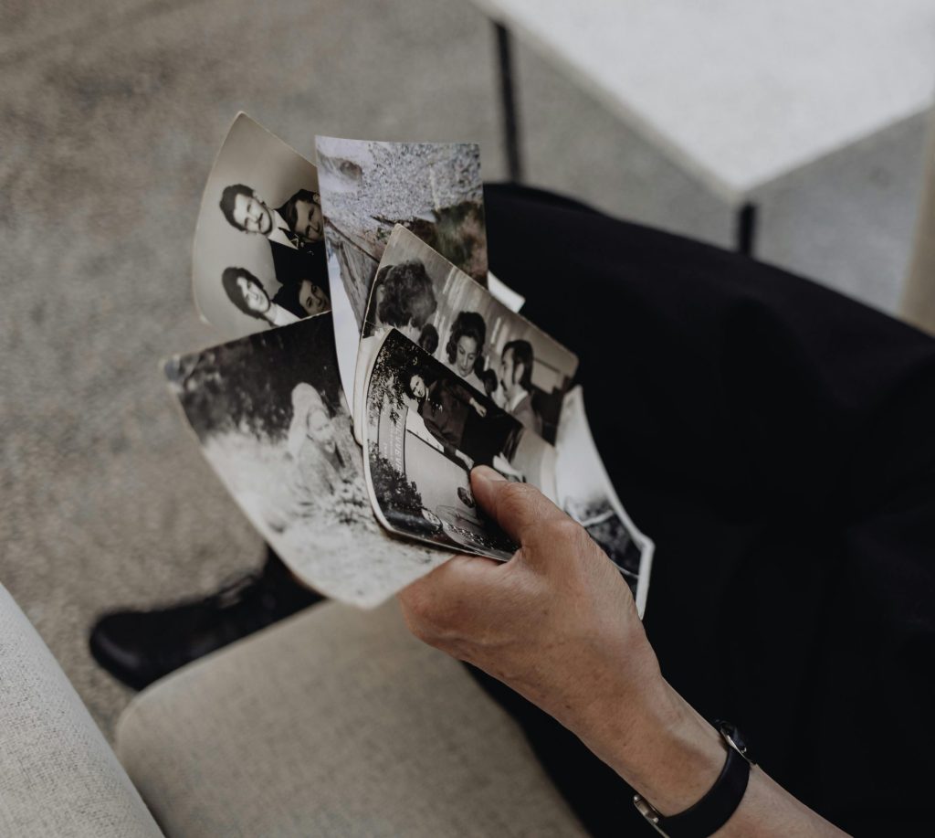 A person reflecting on memories while holding photographs and a wine glass.