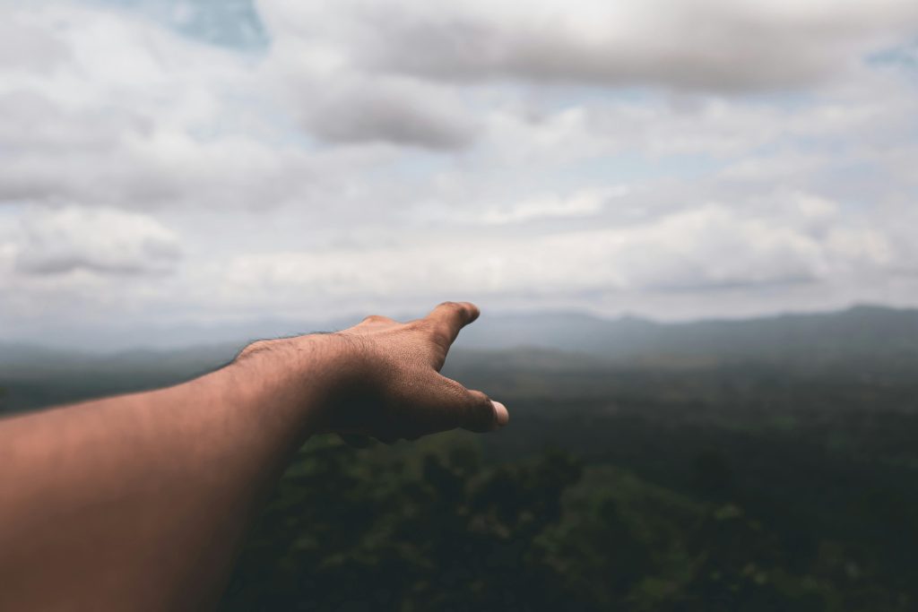 A human hand reaching out towards a misty and cloudy landscape, suggesting exploration and discovery.