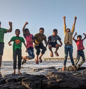 Group of kids joyfully jumping on rocks by the seaside. Fun and playful moment captured outdoors.